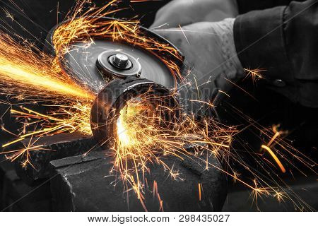 Close-up On The Sides Fly Bright Sparks From The Angle Grinder Machine. A Young Male Welder In A Whi
