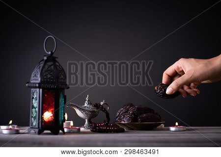 Ramadan Food And Drinks Concept. Woman Hand Reaches Out To A Plate With Date With Ramadan Lantern Wi