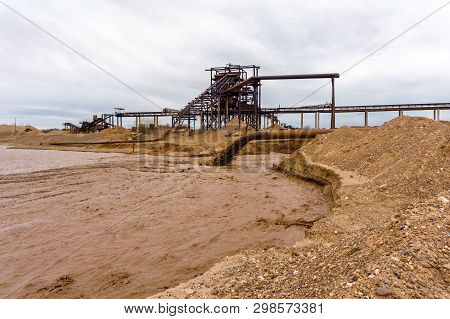 Rusty Pipe On The River Bank, From Which Sewage Flows, Dirty Sand Slurry, And Stationary Rusty Gravi
