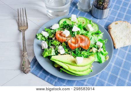 Fresh  Green Salad With Cucumber, Lettuce, Avocado, Tomatoes And Soft Cheese And Glass Water On The 