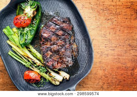 Barbecue dry aged wagyu entrecote beef steak with vegetable and herbs as top view on a gray cast iron pan with copy space right 