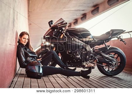 Beautiful Serious Woman Is Sitting Near Her Bike In Tunnel And Leaning On Wall. She Is Holding Helme