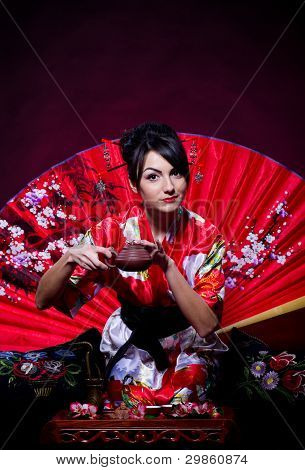 Beautiful young woman in red Asian costume arranging Japanese tea ceremony