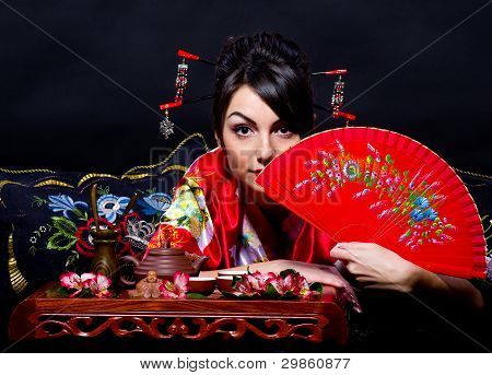 Beautiful young woman in red Asian costume arranging Japanese tea ceremony