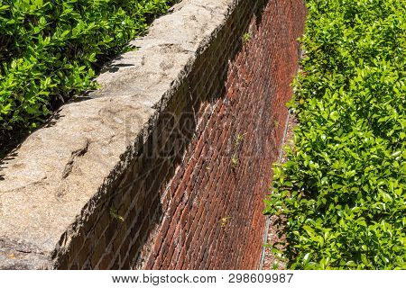 Rusticated Stone Cap On A Red Brick Retaining Wall, Abundant Greenery, Horizontal Aspect