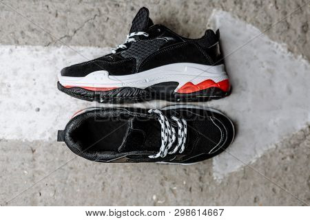 Black Sneakers On A Thick White Sole With Red Accents On A Concrete Background Near A Painted White 