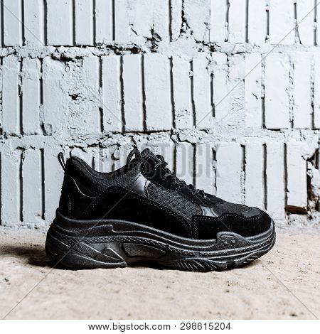 Black Sneaker With Thick Soles On The Cement Floor Against The Background Of Brick Wall