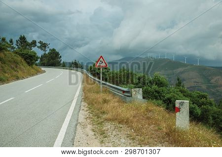 Countryside Paved Road Passing Through Hilly Landscape And Slippery Traffic Signpost, In A Cloudy Da