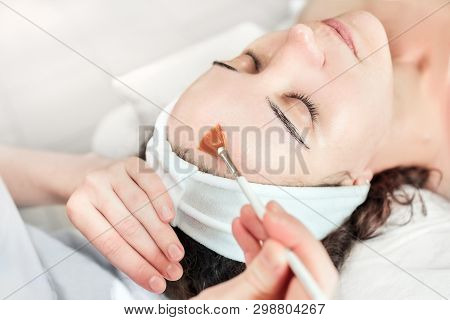 The Cosmetologist Applies Oil (or Phytic Acid) To The Client's Face In The Beauty Salon. A Female Ha