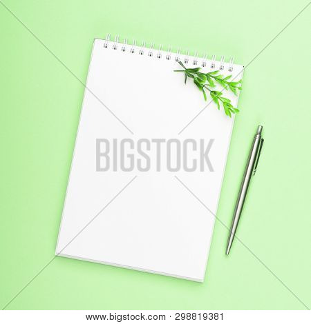 White Notebook With Steel Pen And Green Branches On A Green Background. Office, Spring Composition, 