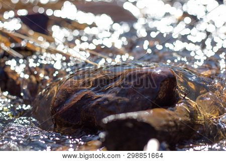 Clean River Water Flows Over The Stones And Envelops Them. Bright Sun Rays Are Reflected In The Flow