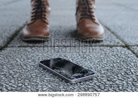 Broken Smartphone With Cracked Screen Glass Lays On A Ground Near Legs Of Young Woman. Girl Crashed 