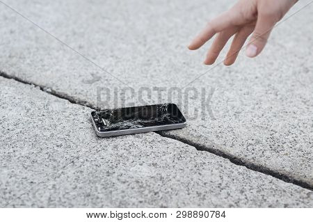 Young Woman Pick Up Her Broken Smartphone With Cracked Screen Glass. Copy Space
