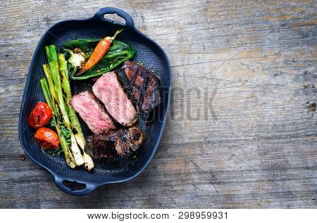 Barbecue dry aged wagyu roast beef steak with vegetable and herbs as top view on a gray cast iron pan with copy space right 