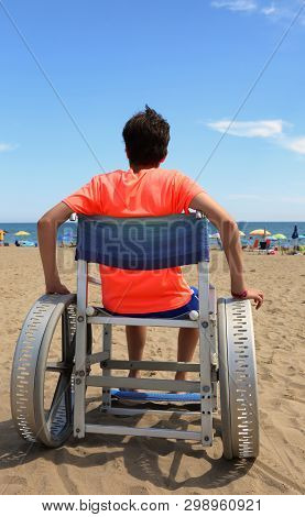 Boy On Wheelchair With Big Aluminum Wheels On The Beach Near The Sea In Summer