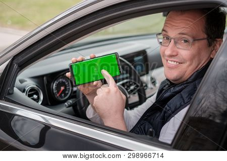 Middle age man shows smartphone with chromakey screen from a car