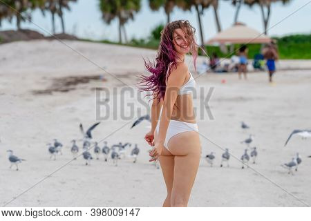 A beautiful brunette bikini model enjoys the weather outdoors on the beach while chasing seagulls