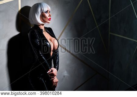 Sexy Woman In A Blonde Wig And Latex Catsuit. Girl With Big Fake Tits