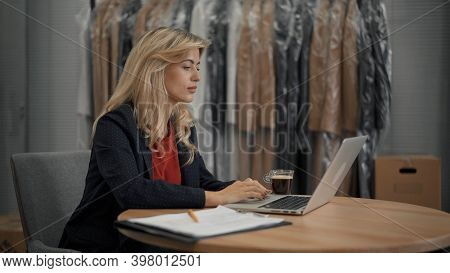 Young Female Manager With Laptop On Background Of Coats On Hangers In Design Studio. Young Female Ma