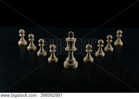 Chess King With A Retinue Of Pawns On A Black Background. The Concept Of A Leader And His Followers.