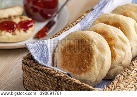 English Muffins In A Basket With A Muffin And Preserves In Background On A Wooden Table