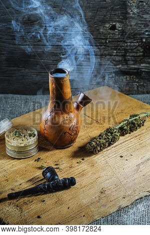 Old Brown Steamung Bong And Open Cannabis Grinder With Chopped Marijuana Weed And Medical Cannabis I