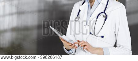 Unknown Woman Doctor Iusing Tablet Computer In Her Hands, While Standing In Clinic. Medicine Concept