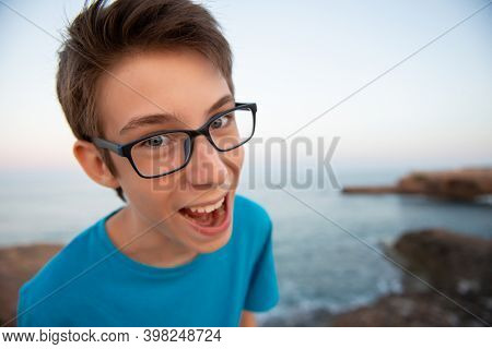 Funny young happy teen boy makes faces with open mouth at beach at the evening, wide angle. 