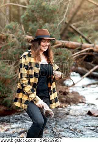 Woman In Yellow Shirt And Hat Walking Along The River In The Autumn Forest
