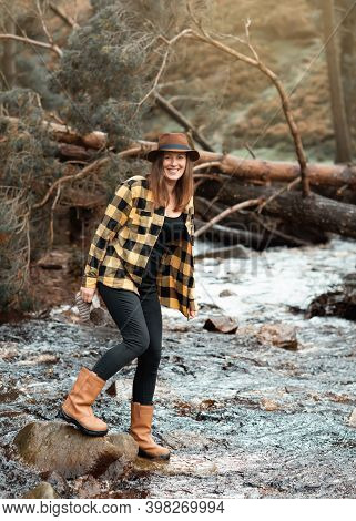 Woman In Yellow Shirt And Hat Walking Along The River In The Autumn Forest