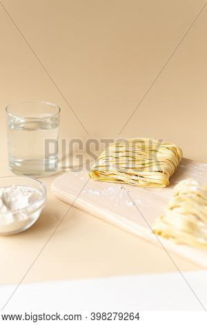 Natural Homemade Noodles With Flour And A Glass Of Water On A Brown Background. Vertical Orientation