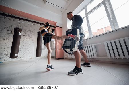 Training Of A Professional Female Fighter. The Girl Works Out A Kick On The Paw, Which Is Held By He