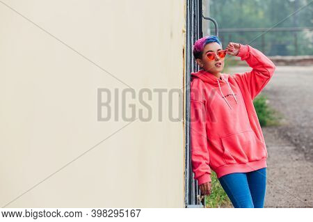 Portrait Of A Young Girl With Short Colorful Hair And Nose Piercing Satanding Near The Wall With Woo