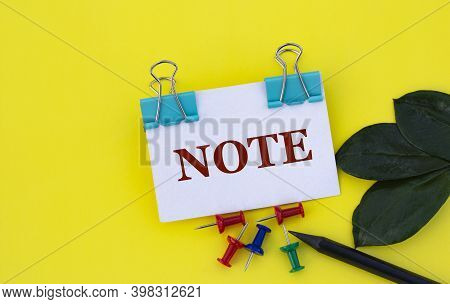 Note - Word On A White Sheet With Clips On A Yellow Background With Buttons, A Green Sheet And A Pen