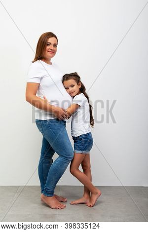 Pregnancy. Happy Family Expecting Baby. Beautiful smiling girl hugs her pregnant mother with big belly. Indoor portrait of mom and daughter.