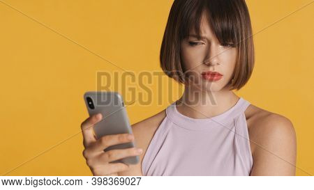 Upset Girl With Unhappy Expression Didnt Get Message From Boyfriend Using Smartphone Isolated On Yel