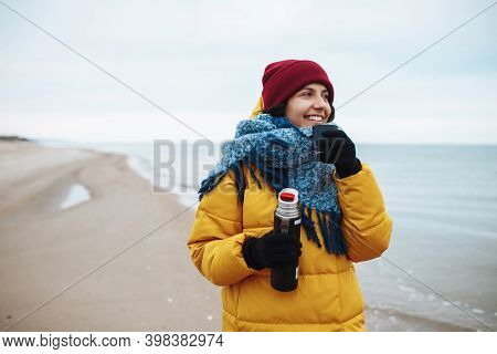 Young Woman Pours Hot Tea From A Thermos Into A Cup And Drinks On The Seaside. Female Tourist Is Hav