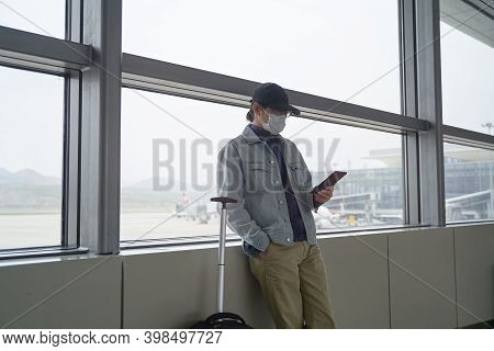Young Asian Man Male Air Traveler Reading E-book Using A E-reader While Waiting For Boarding In Airp