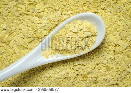 closeup of nutritional organic yeast flakes - background and texture with a white teaspoon, nutrition supplement, baking and cooking