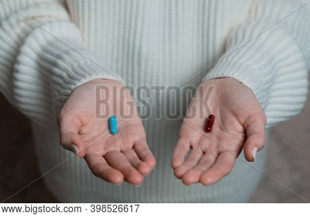 Hands Of A Female In A White Sweater Offer A Choice Two Opposite Colorful Pills. Blue And Red Candy 