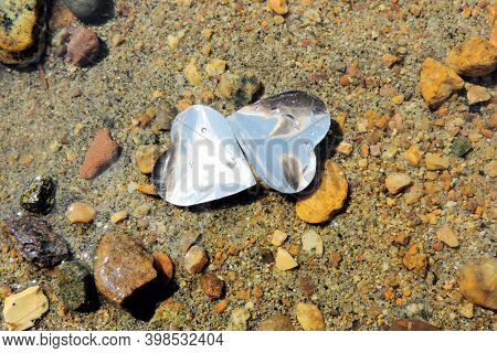 Two Hearts And Silver Foil Float On The Surface Of The Water In The River, The Background Is Rocky B