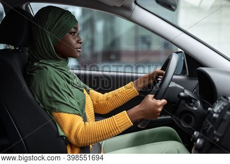 Young Driver. Serious Black Muslim Lady In Hijab Driving Car, Holding Steering Wheel And Looking Ahe