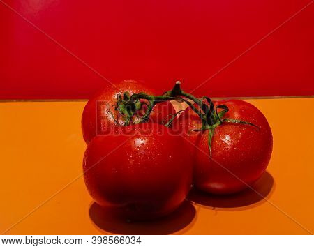 Round Red Tomatoes On A Branch With A Colored Background And Water Drops