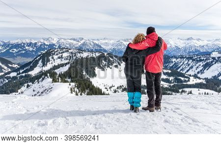 Senior Couple Is Hiking In Alpine Snow Winter Mountains Enjoying Panorama View. Allgau, Bavaria, Ger