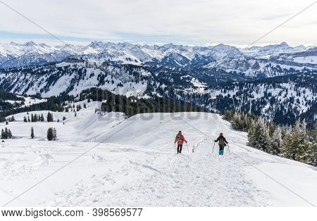 Senior Couple Is Snowshoe Hiking In Alpine Snow Winter Mountains. Allgau, Bavaria, Germany.