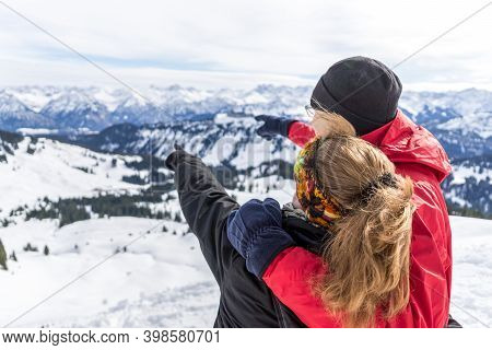 Senior Couple Is Hiking In Alpine Snow Winter Mountains Enjoying Panorama View And Pointing With Fin