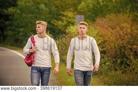 Twins Walk Along Road. Adventure Concept. Guys Hitchhiking On Road. Tourist Traveler Travel Auto Sto