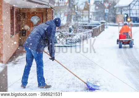 Man With Snow Shovel Cleans Sidewalks In Winter During Snowfall. Winter Time In Europe. Young Man In
