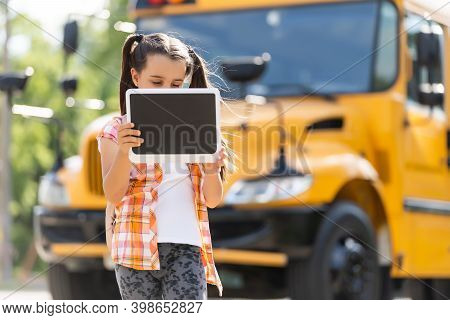 Adorable Little Schoolgirl Near School Bus And Looking At Camera