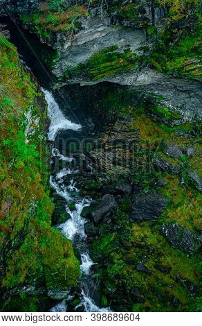 Waterfall Running Through A Deep Gorge Surrounded By Lush Green Vegetation. Seen From Above.